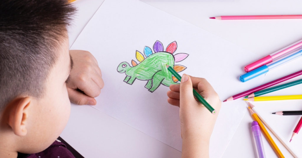 A boy draws a dinosaur with colored pencils and markers on white paper. children's drawings, children's creativity